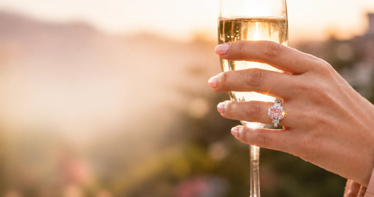 woman's hand holding champagne with a pink diamond ring